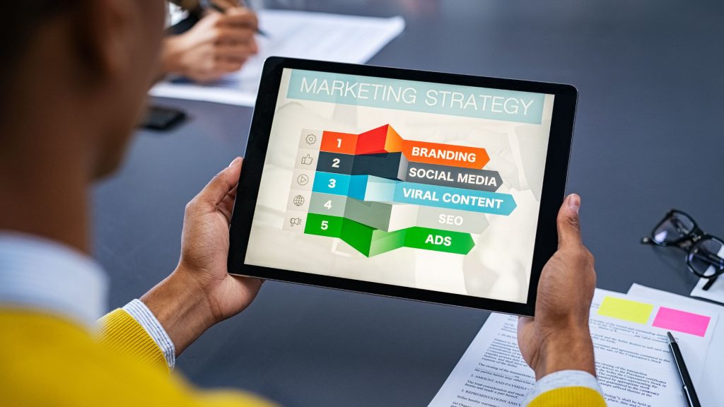 Promotion - man holding a tablet on which you can see 5 different elements of a marketing strategy